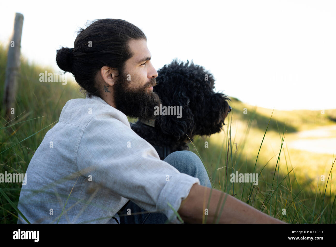 Junge Mann in den Dünen mit seinem Hund sitzen Stockfoto