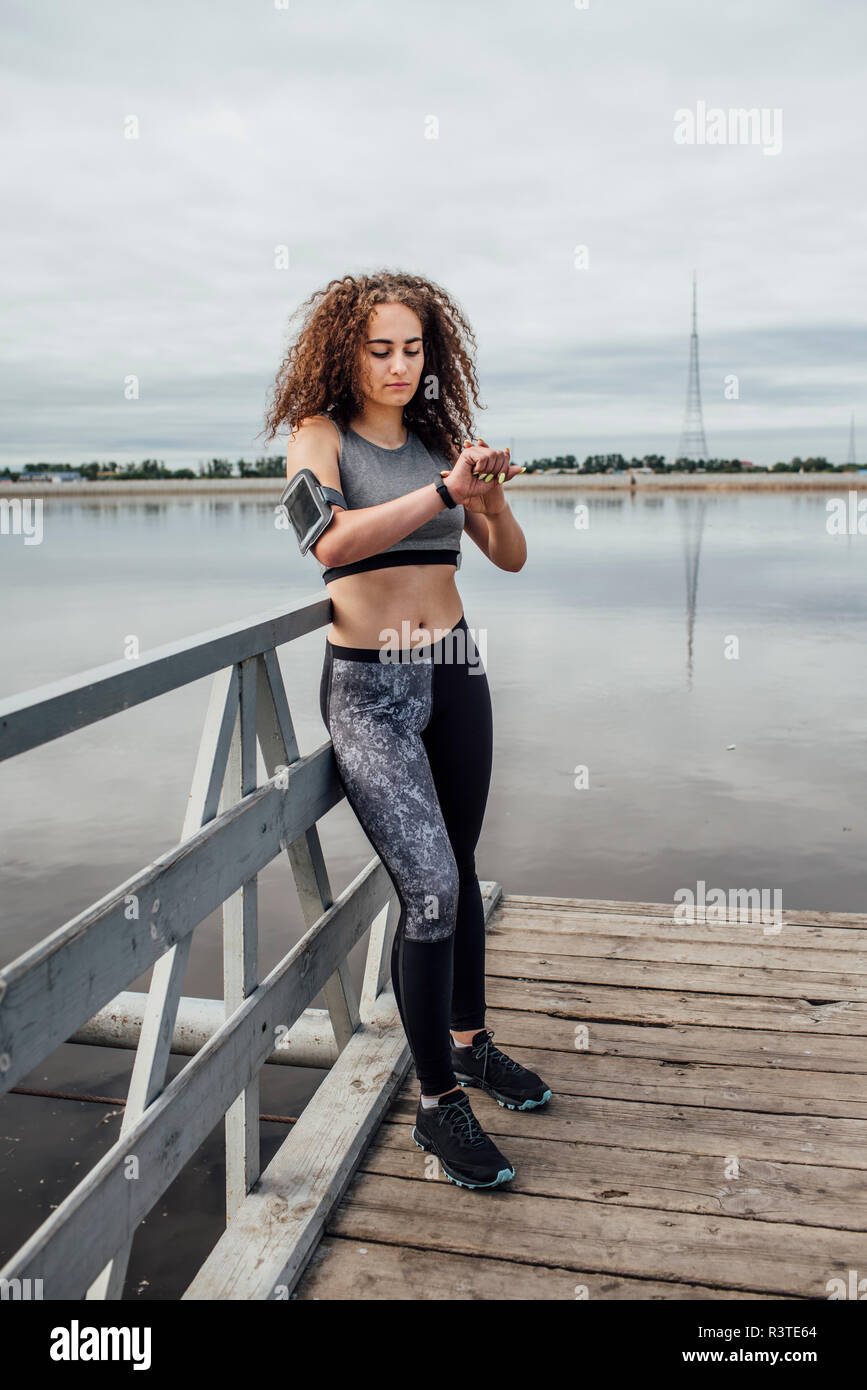 Junge athletische Frau am Flußufer an Armbanduhr suchen Stockfoto