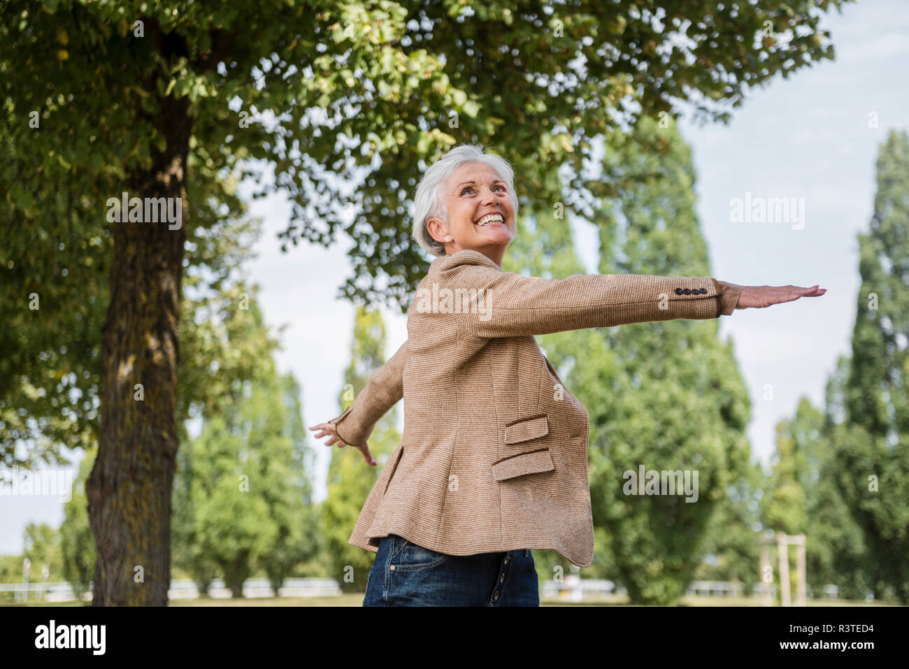 Gerne ältere Frau mit ausgestreckten Armen in einem Park Stockfoto