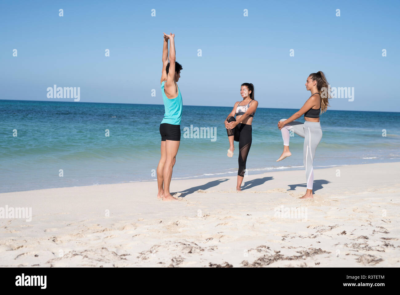 Spanien, Kanarische Inseln, Fuerteventura, zwei junge Frauen und ein junger Mann am Strand trainieren Stockfoto