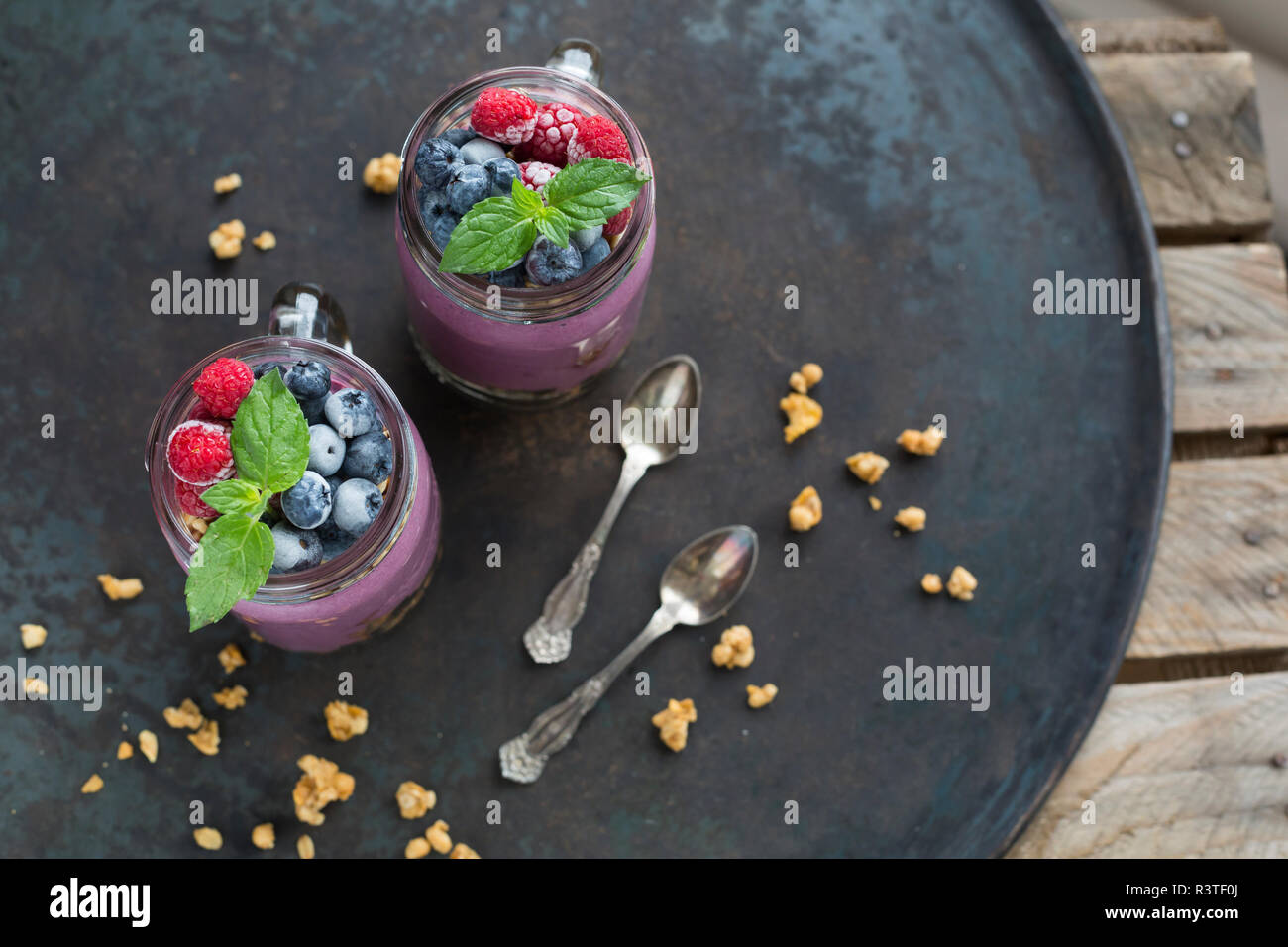 Zwei Gläser Joghurt mit Erdnuss Müsli, aronia Pulver und Nachfüllen von gehackten Haselnüssen und Gefrorene Beeren Stockfoto