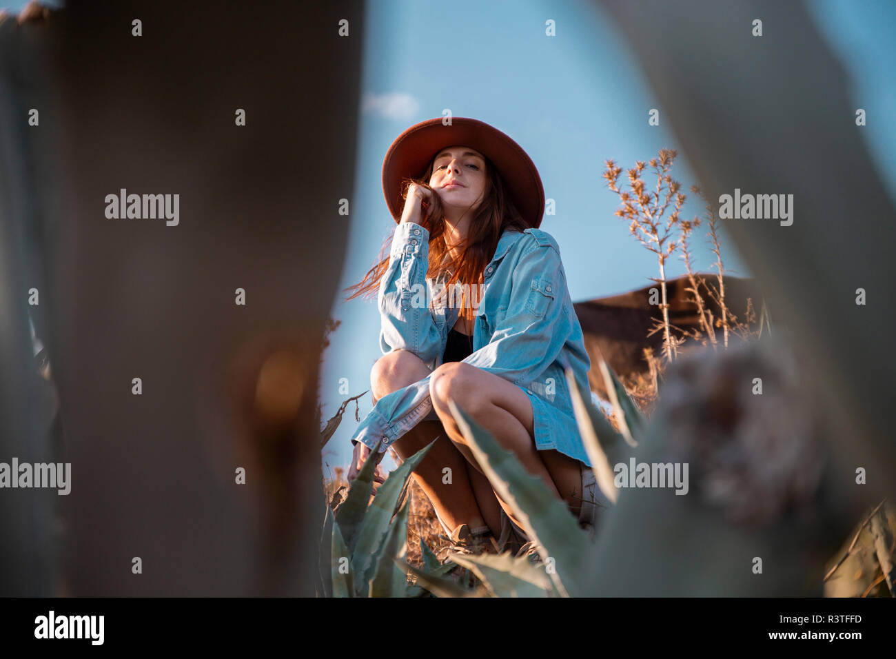 Junge Frau mit Hut sitzt in einer Agave in ländlicher Welt Stockfoto