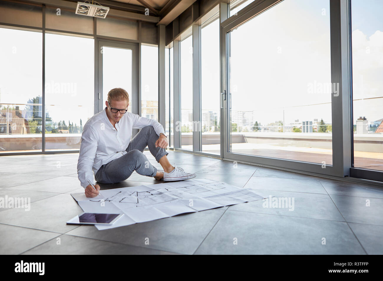 Junger Mann sitzt im leeren Raum mit Panorama fenster Arbeiten an Blueprint Stockfoto