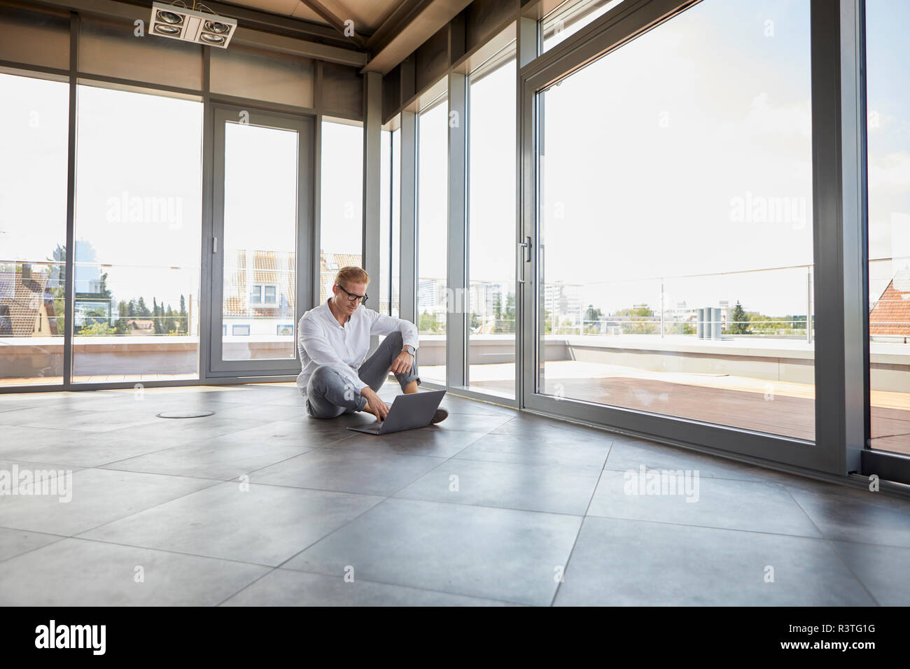 Geschäftsmann sitzt im leeren Raum mit Panorama Fenster mit Laptop Stockfoto