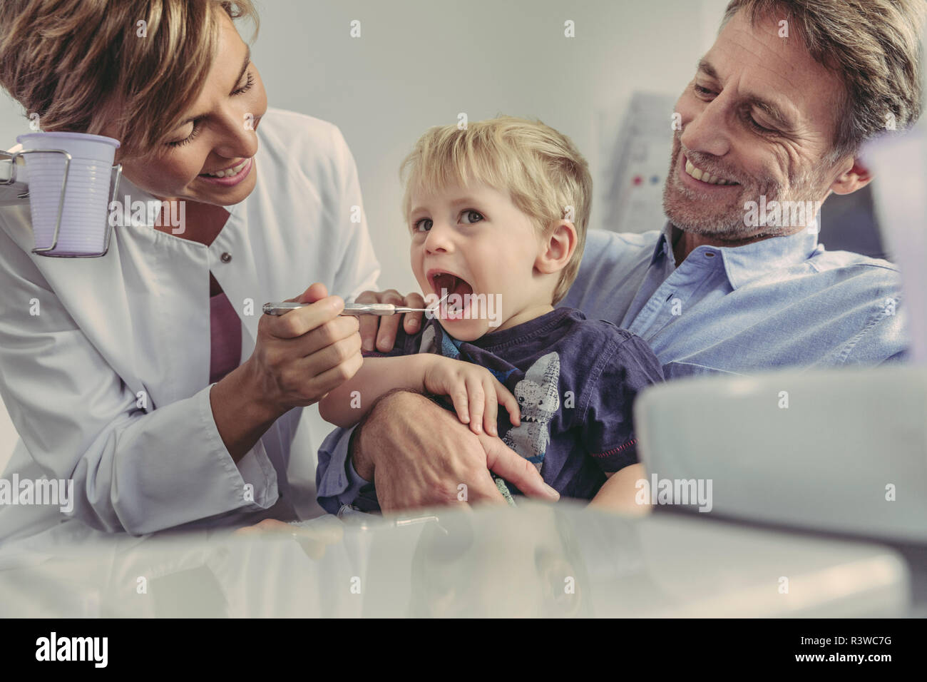 Weiblichen Zahnarzt Prüfung kleiner Junge sitzt auf dem Schoß seines Vaters Stockfoto