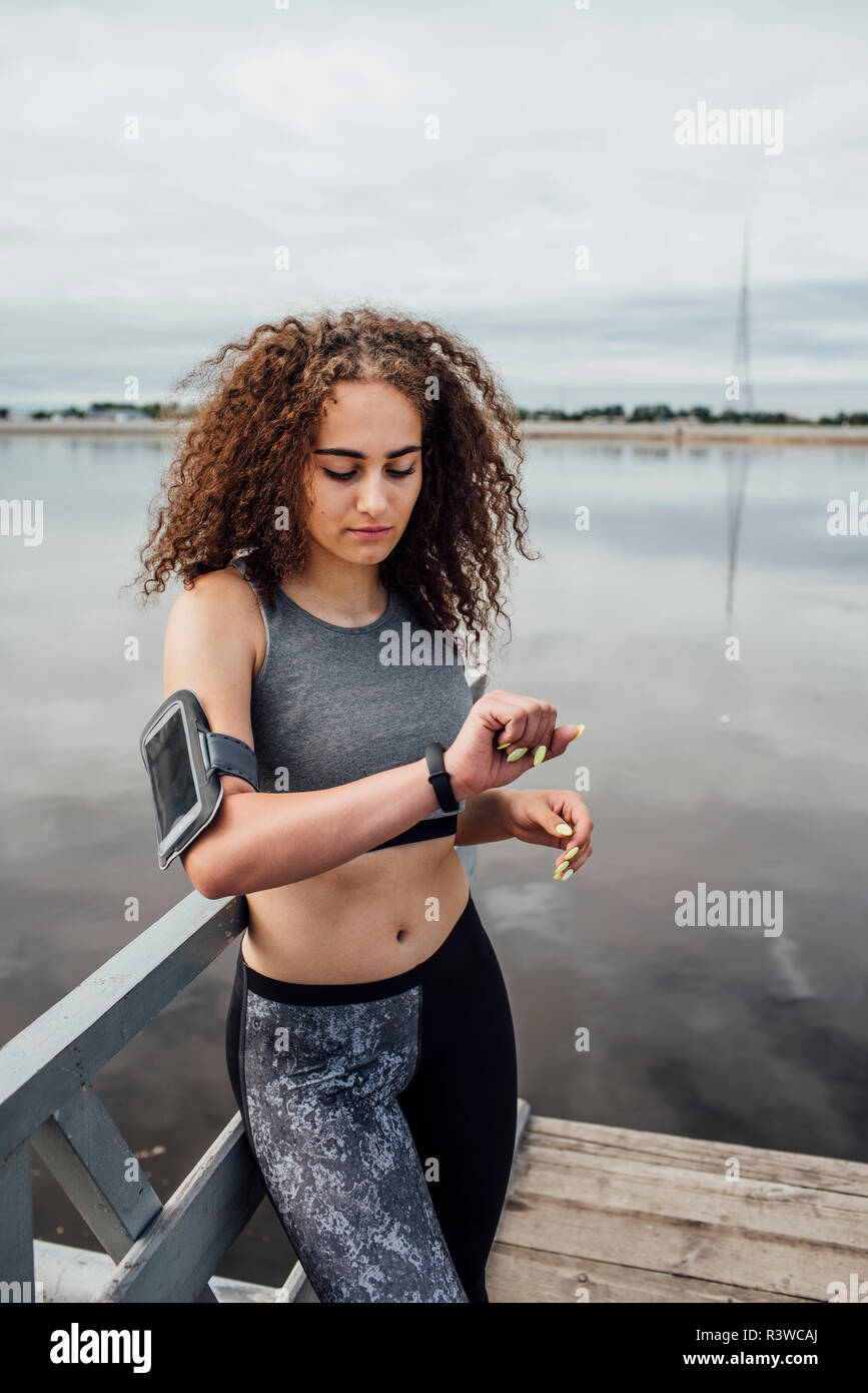 Junge athletische Frau am Flußufer an Armbanduhr suchen Stockfoto