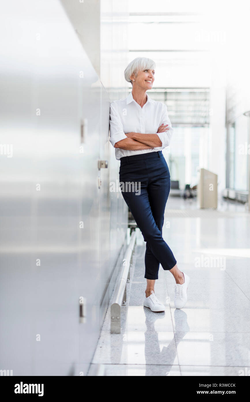Lächelnd senior Geschäftsfrau gegen eine Wand gelehnt Stockfoto