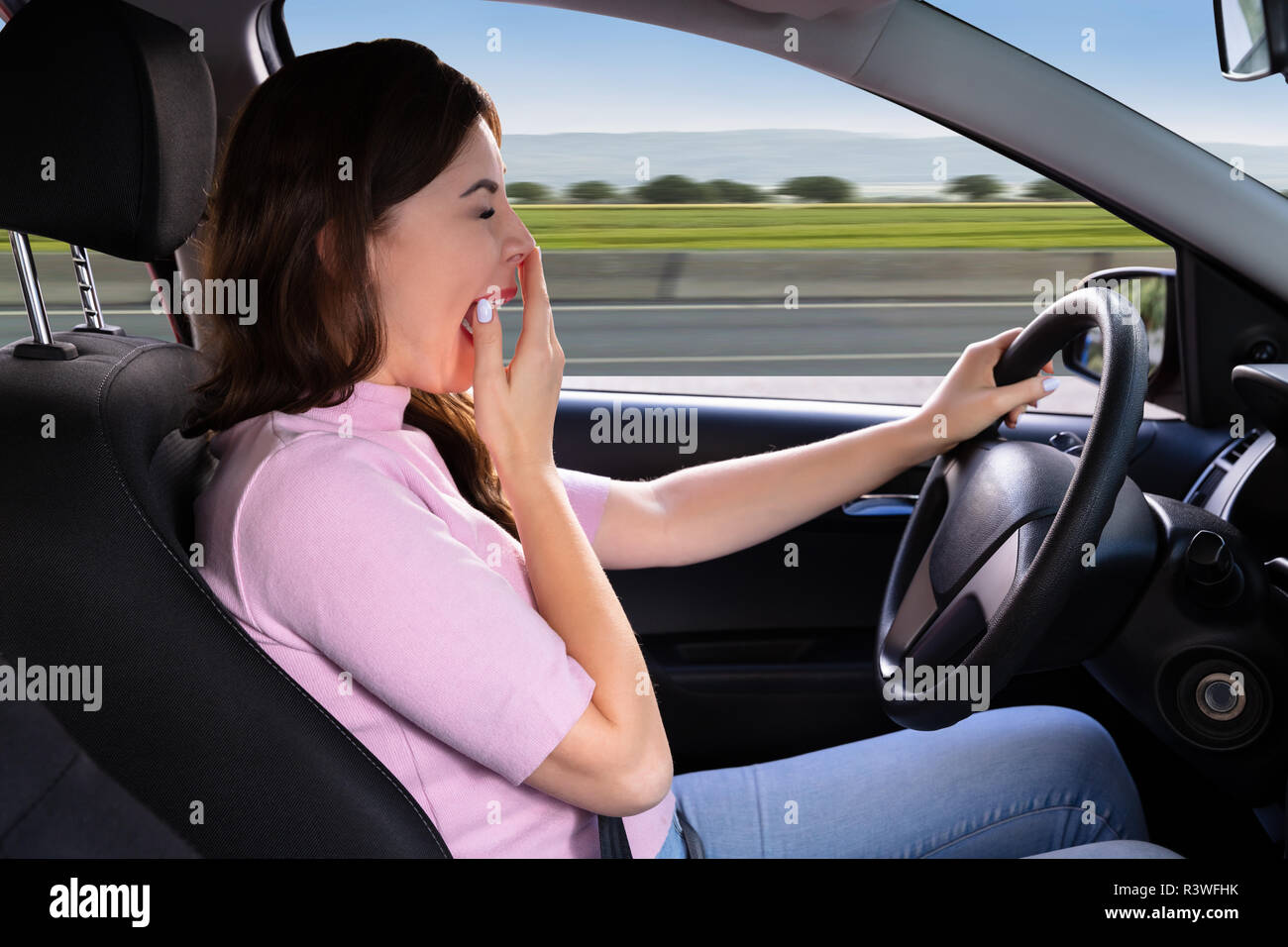 Seitliche Sicht auf eine schöne junge Frau Gähnen während der Fahrt Auto Stockfoto