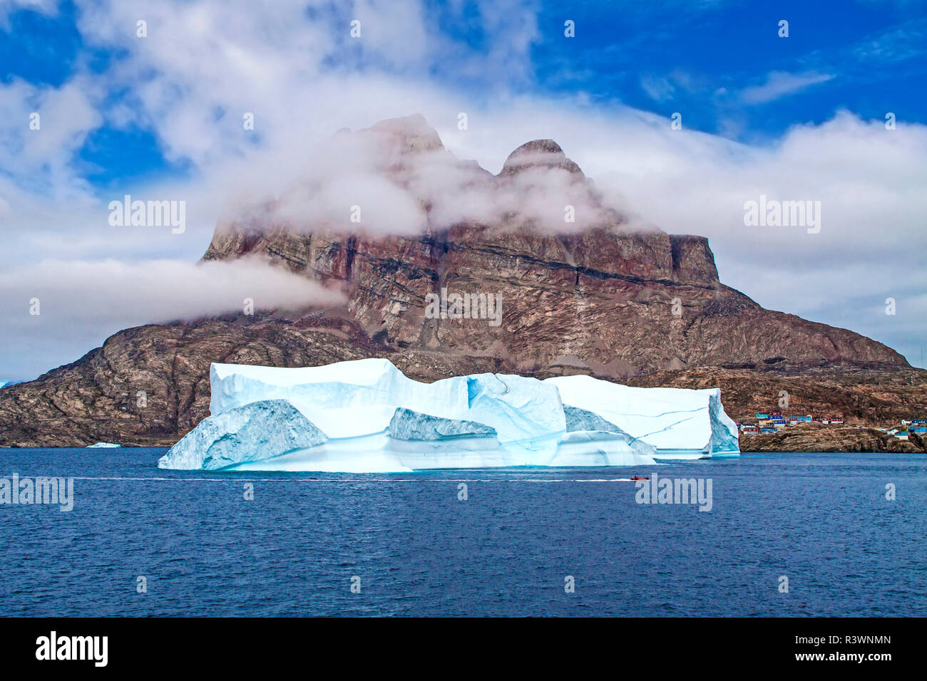 Grönland, Uummannaq. Eisberg schwebt durch die Hafen- und Fischerdorf Uummannaq zusammen mit Uummannaq Berg Stockfoto