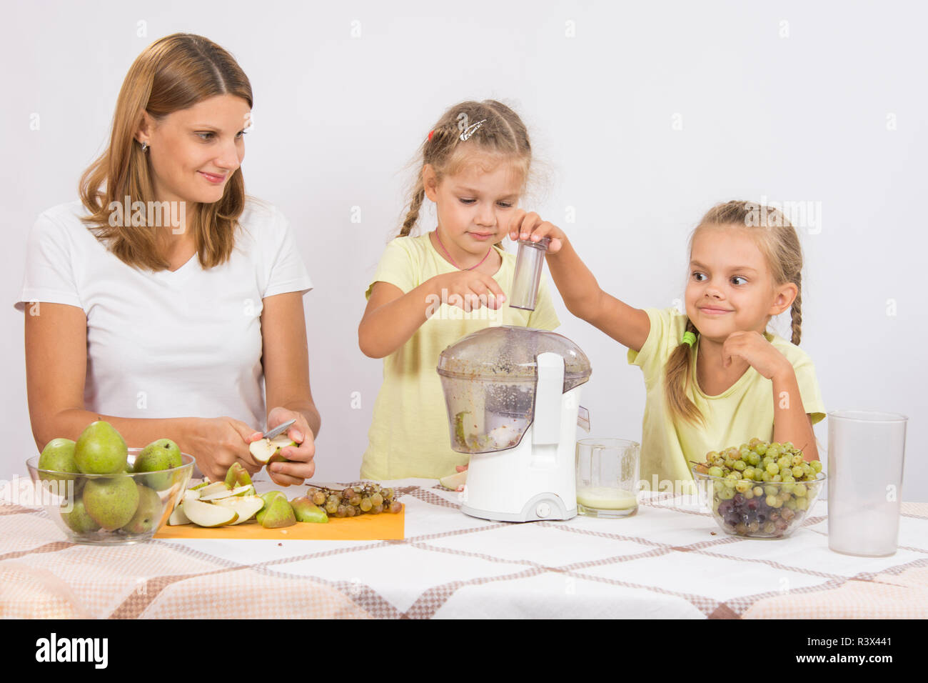Kinder werfen die Frucht in einem Entsafter in der Obhut der Mütter Stockfoto