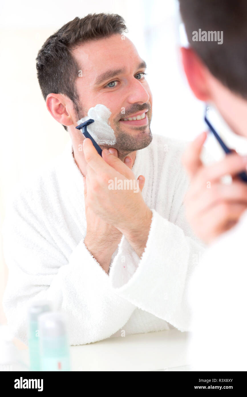 Jungen attraktiven Mann rasieren sich den Bart vor einem Spiegel Stockfoto