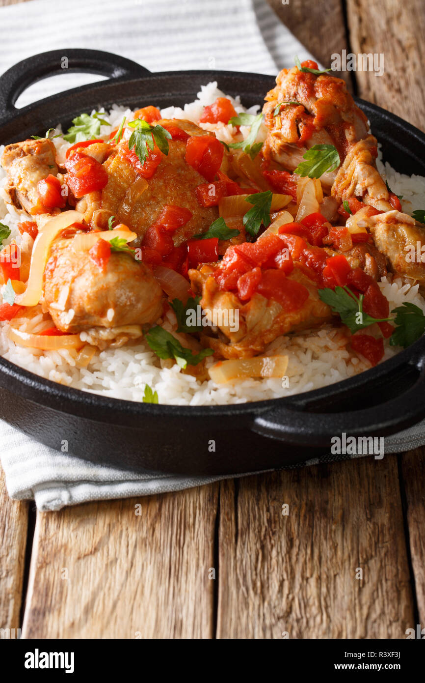 Haitianische Hühnchen in einer würzigen Tomatensauce mit Reis Beilage close-up in einer Pfanne auf dem Tisch. Vertikale Stockfoto