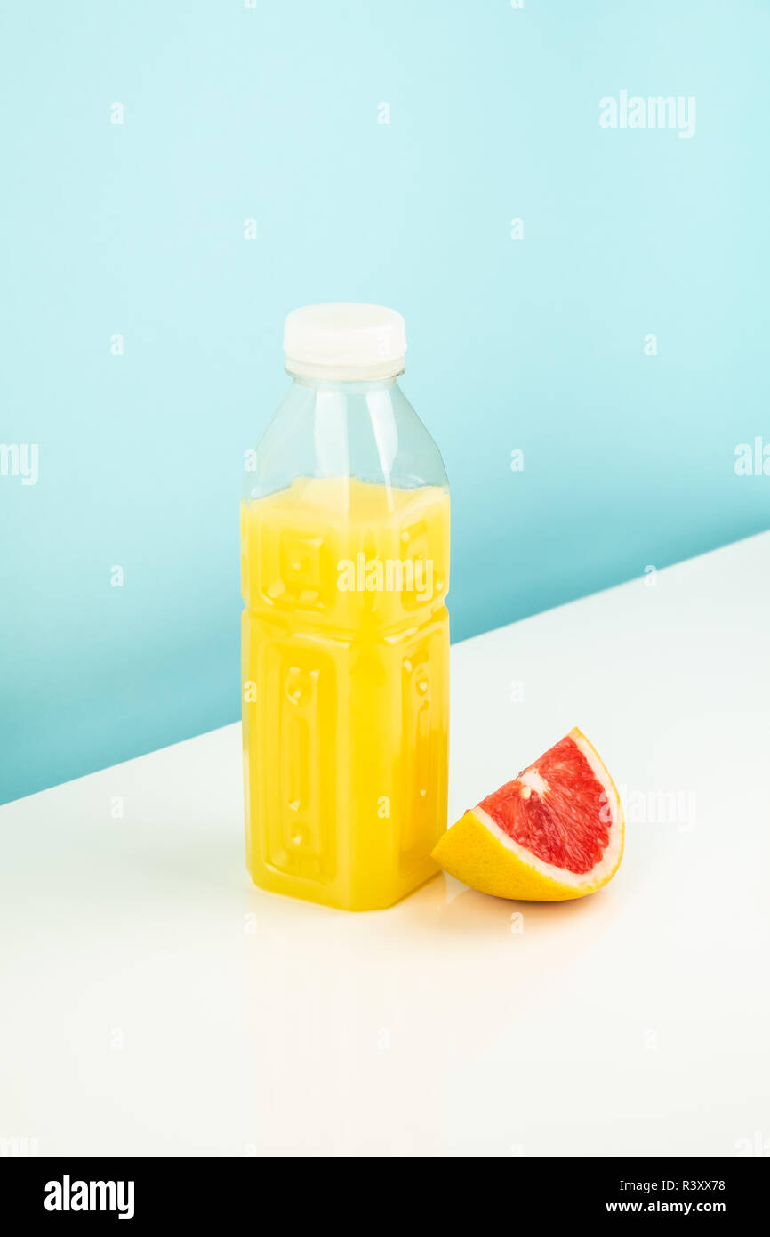 Orange Getränk und ein Stück Grapefruit auf Weißem und Blauem Hintergrund. Minimalistischer Bild von Citrus Flasche Saft und Obst bei der Spärlichen hell. Stockfoto
