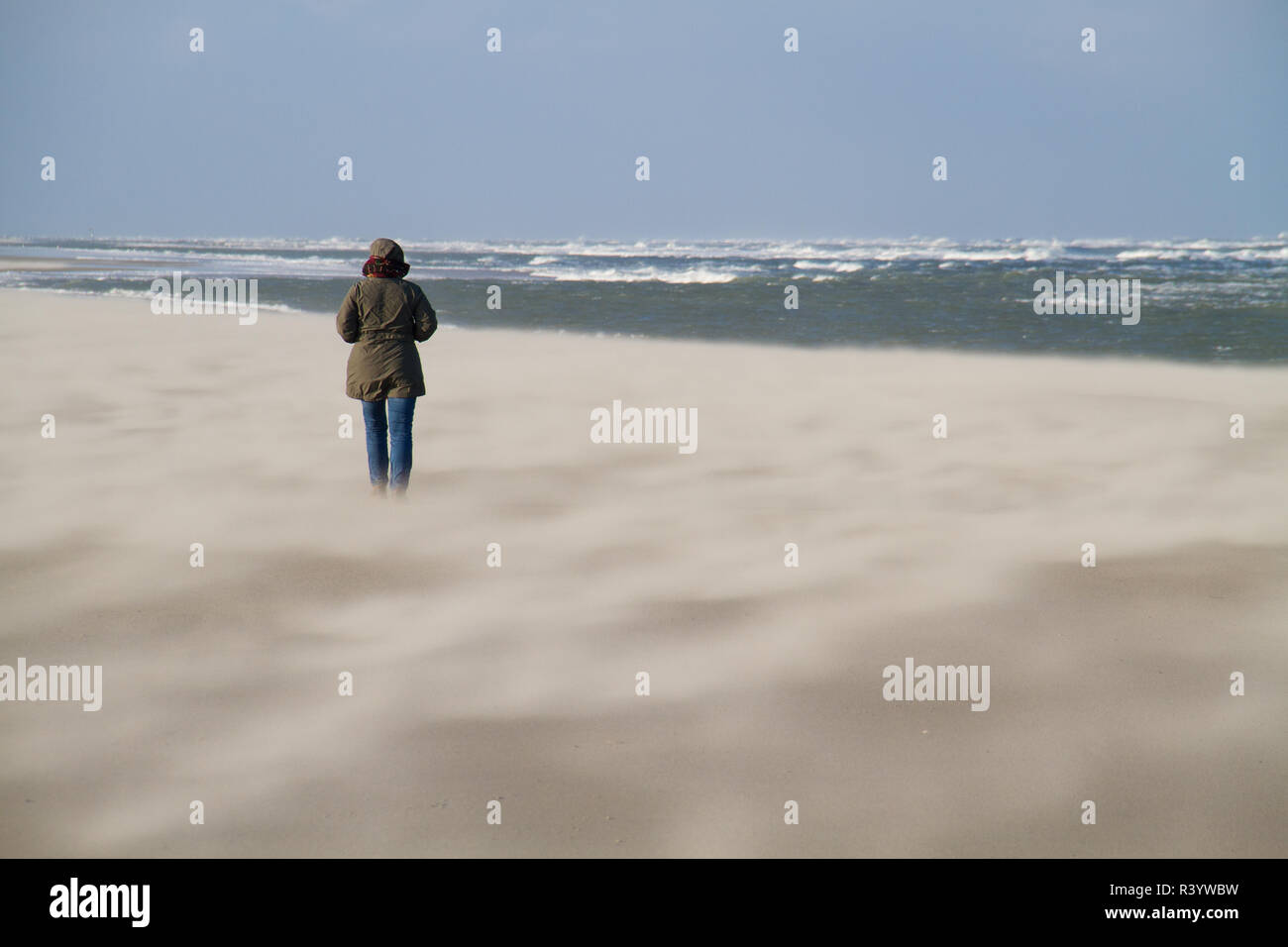 Frau zu Fuß am Strand an einem stürmischen Tag im Winter, Sand über den Strand Stockfoto