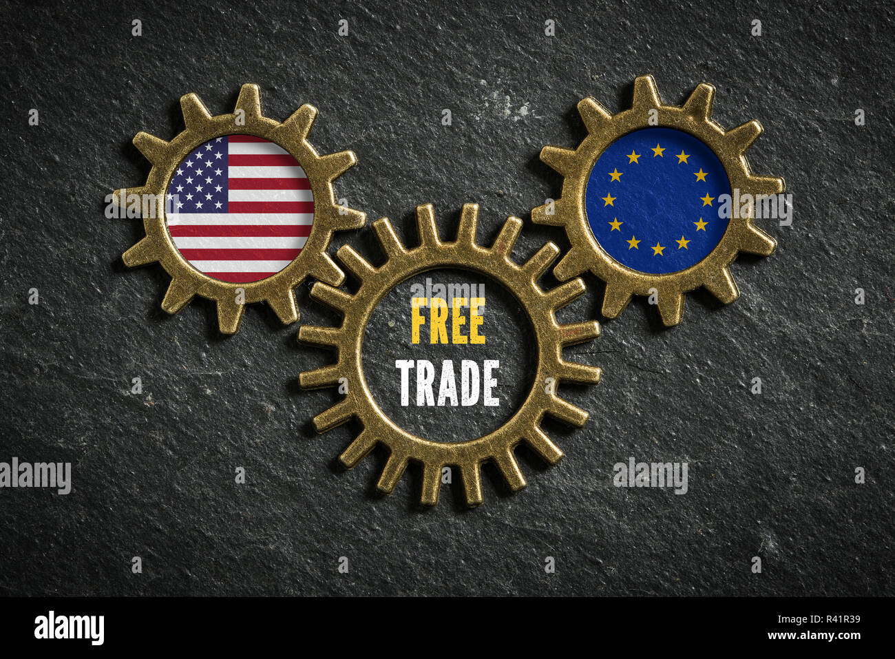 Drei Zahnräder auf schiefer Hintergrund mit den Flaggen der USA und der EU und die Worte 'Freihandel' in der Mitte Stockfoto