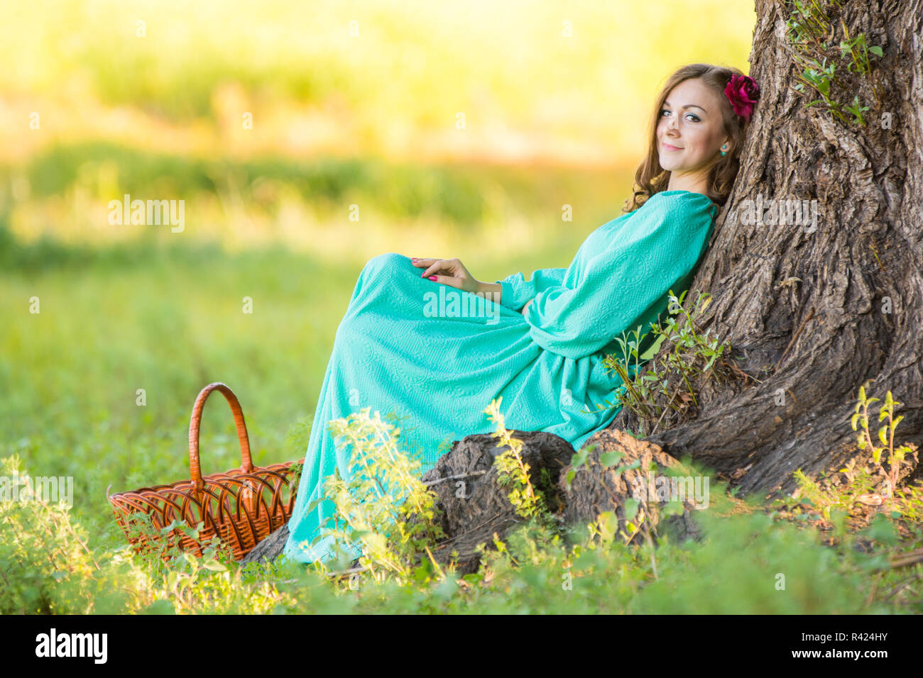 Eine Mädchen in einem langen Kleid setzte sich an den alten Baum im Wald Stockfoto