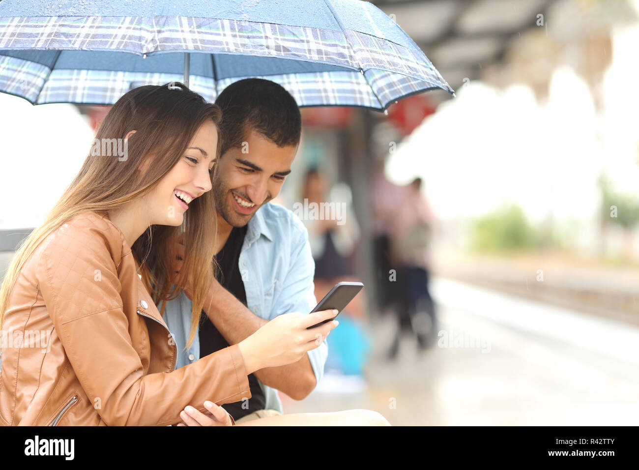 Interracial Paare teilen ein Telefon in einem Bahnhof Stockfoto