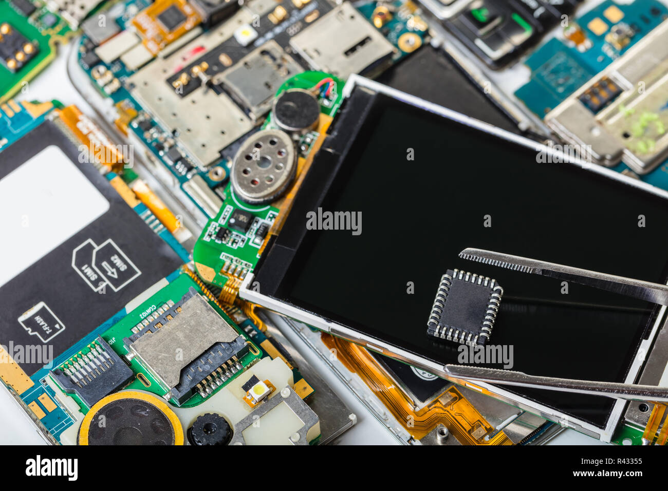 Elektronische chip in Pinzette auf dem Hintergrund der demontierten Mobiltelefon Stockfoto