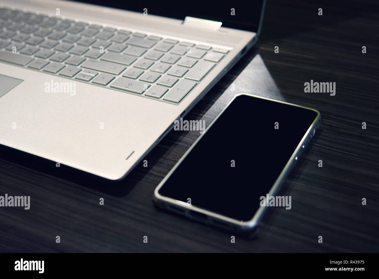 Smart Phone mit Copy space Screen und Laptop auf hölzernen Tisch Hintergrund. Leeren schwarzen Bildschirm eines mobilen links auf dem Tisch in der Nähe des Computers. Nutzung digitaler Geräte bei der Arbeit. Telefon Display mockup. Stockfoto