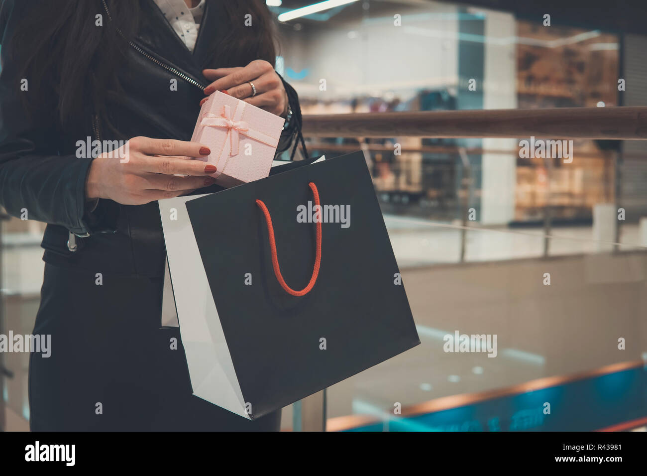 Geschenk Taschen in den Händen der Mädchen, auf dem Hintergrund, Shopping Mall. Shopping, Geschenke, Verkauf, shopping. Frau setzt eine Geschenkverpackung in einem schwarzen Gehäuse. Stockfoto