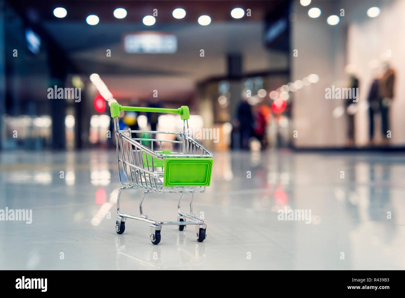 Eine kleine grüne Spielzeug Warenkorb in einem großen Einkaufszentrum. Das Konzept der Einkauf und Verkauf in Supermärkten. Blur Warenkorb im superstore. Stockfoto