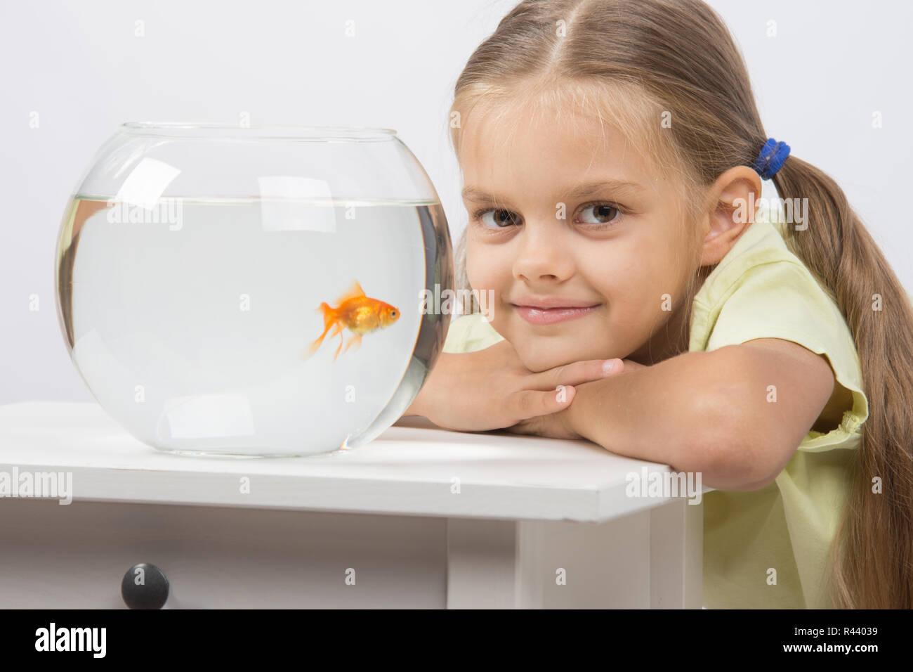 Sechs Jahre altes Mädchen legte den Kopf auf dem Handgriff sitzen am Tisch mit einem Aquarium mit Goldfischen Stockfoto