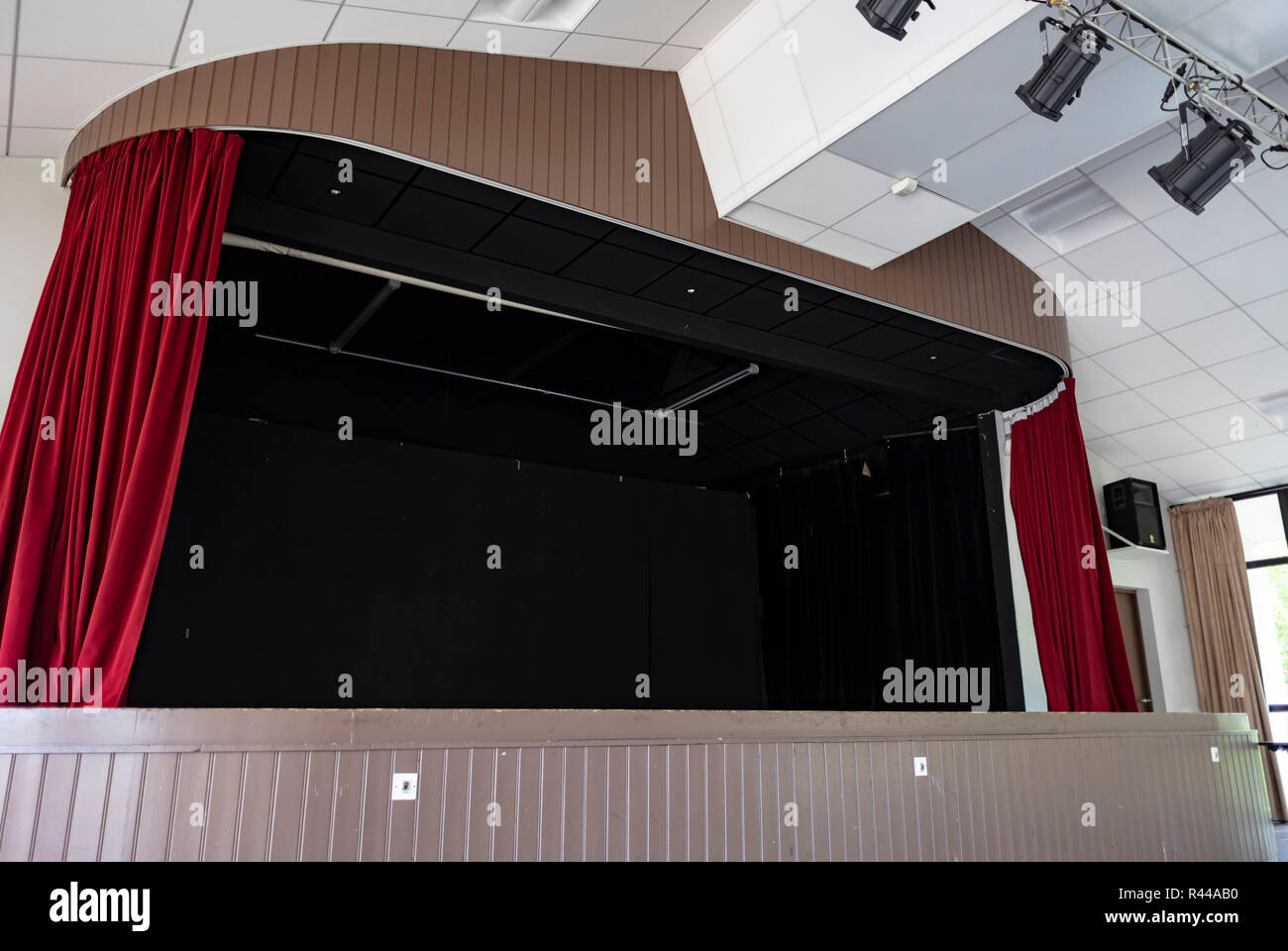 Weite Einstellung auf ein Innen schwarze Bühne mit roten Vorhängen und Scheinwerfer an der Decke hing, mit Holztäfelung umgeben. Stockfoto