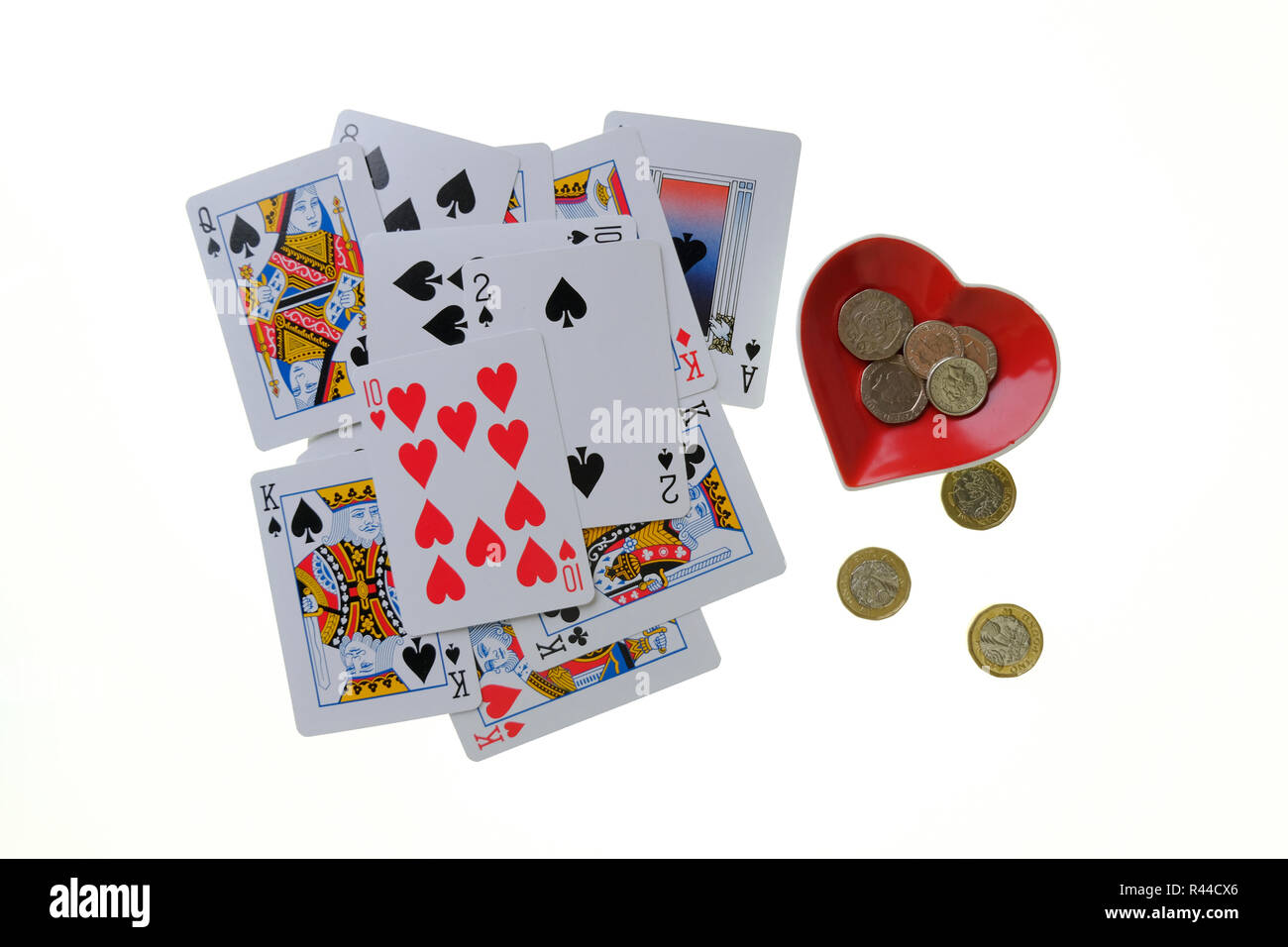 Stapel der traditionellen Spielkarten auf weißem Hintergrund mit Herz Ass geformte Schmuckstück Schüssel auf die Seite mit Loose Change in und neben ihm. Stockfoto