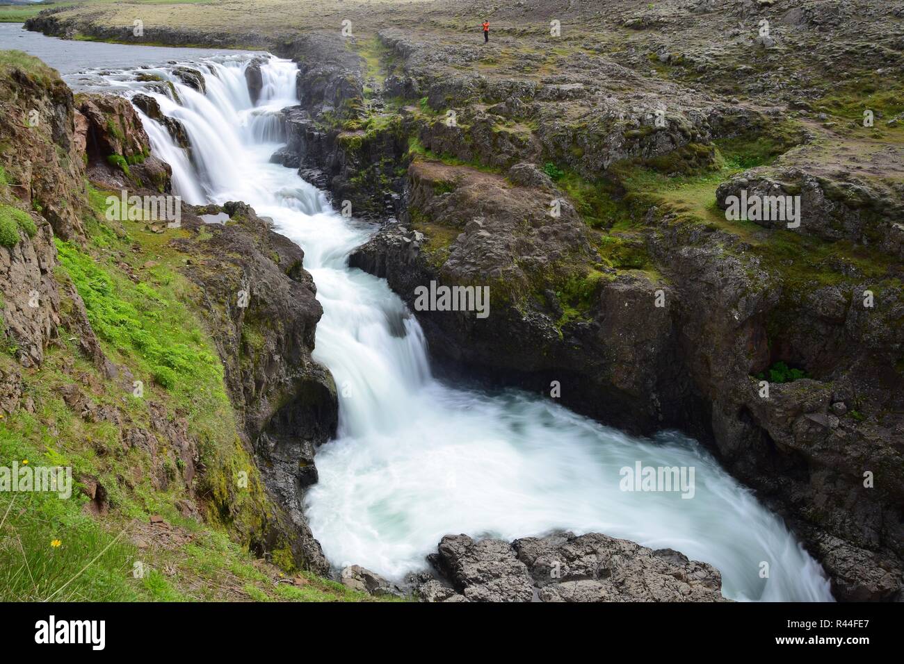 Kolufossar, einem Wasserfall im Nordwesten Islands an der Kolugljufur Canyon. Lange Belichtung. Im oberen Teil ist eine kleine Person in einem orange Jacke. Stockfoto