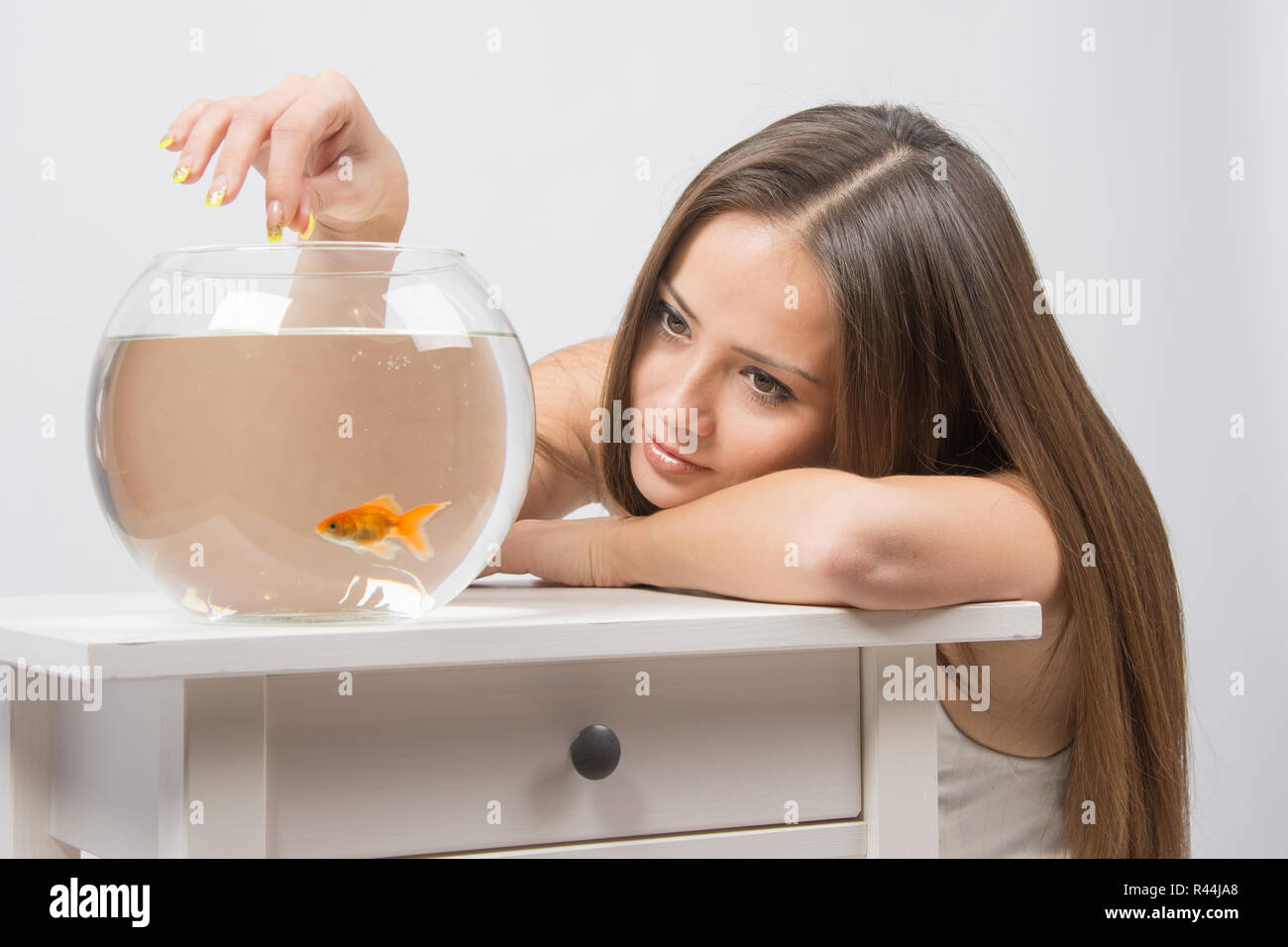Junges Mädchen legte den Kopf auf seine Hand, die andere Hand füttert die Fische im aquarium Stockfoto