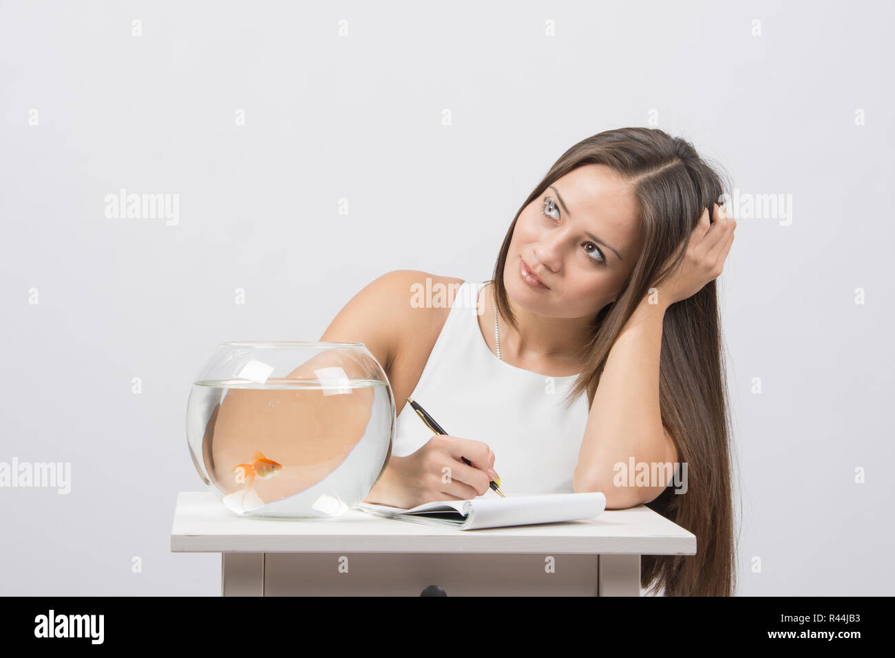 Mädchen schreiben sorgfältig in einem Notebook, stehen neben einem Aquarium mit Goldfischen Stockfoto