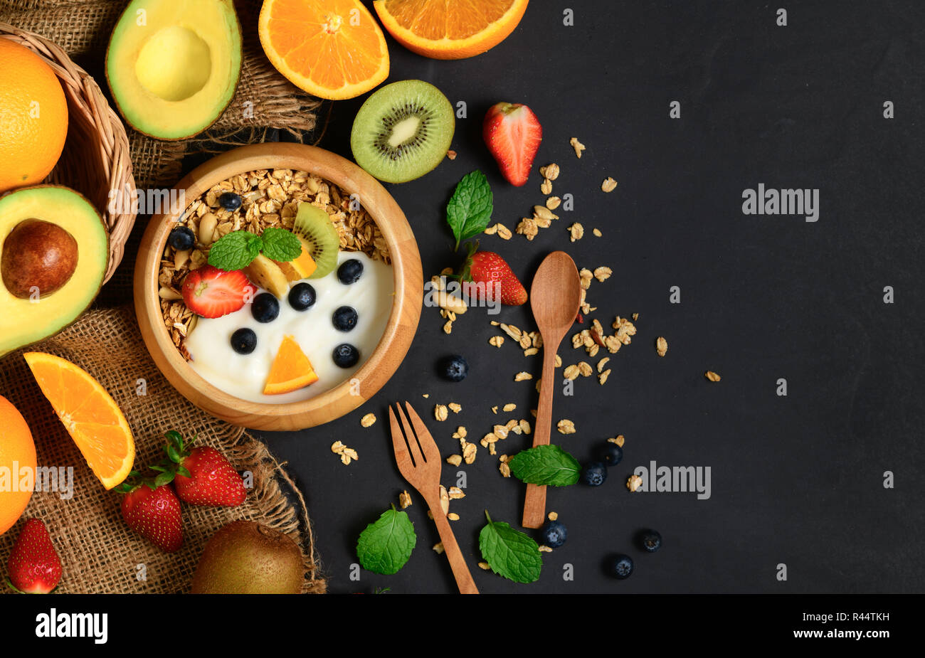 Müsli und Joghurt mit Früchten in Holz Schüssel und Früchte auf schwarzen Steintisch, gesunde Ernährung Konzept Stockfoto