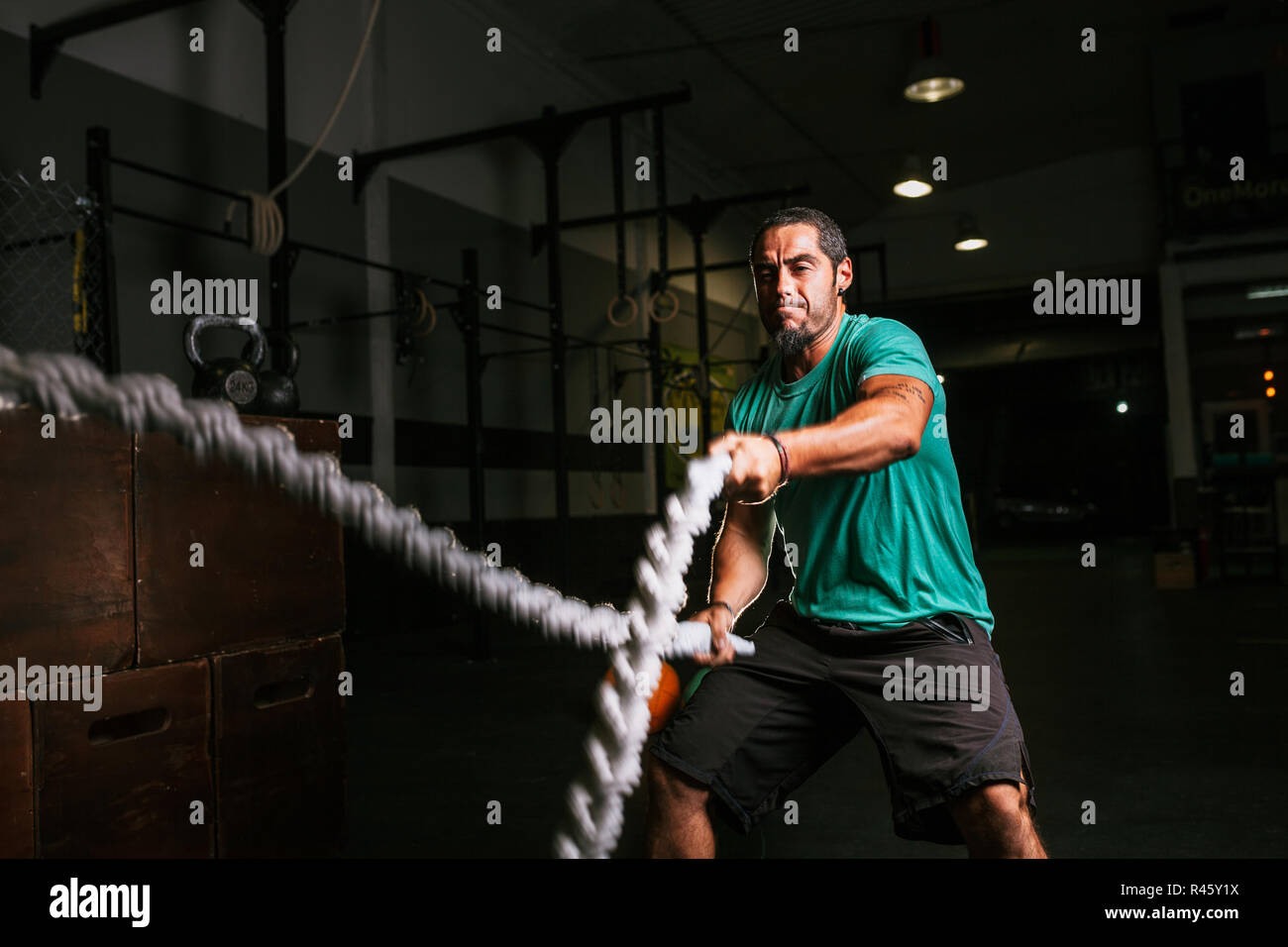 Athletischen jungen Mann dabei einige cross-fit Übungen mit einem Seil indoor Stockfoto