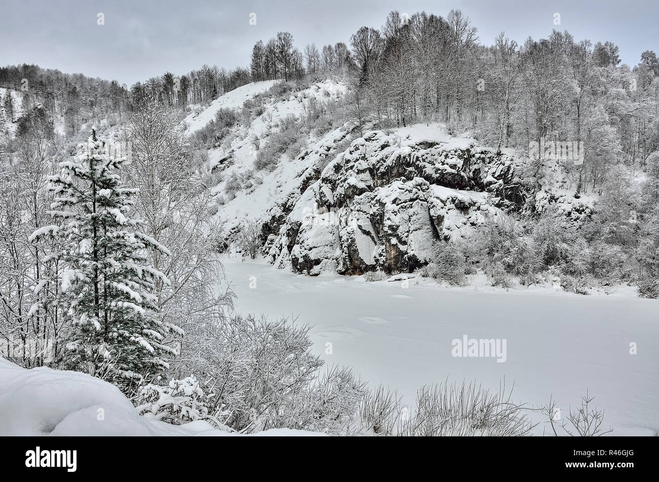 Winterlandschaft von gefrorenen mountain river mit felsigen Küsten. Hänge der Berge mit schneebedeckten Wald bedeckt. Tannenbaum und Schneeverwehungen auf foregro Stockfoto
