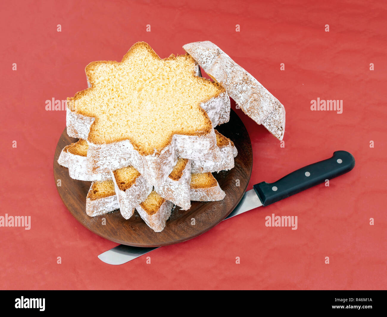 In Scheiben geschnitten Pandoro, süßen italienischen Hefe Brot, traditionelle Weihnachten behandeln. Mit Messer auf Rot. Overhead flach anzeigen. Stockfoto