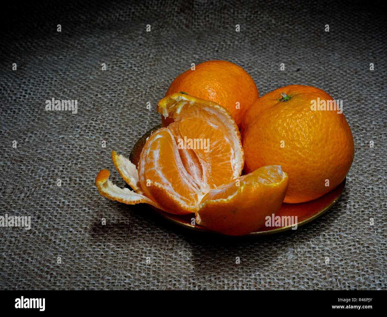 Mandarin oder Clementinen, Orangen, dunklen Stillleben auf rustikalen Hessischen. Licht Maltechnik. Drei Obst, ein Teil abgezogen. Stockfoto