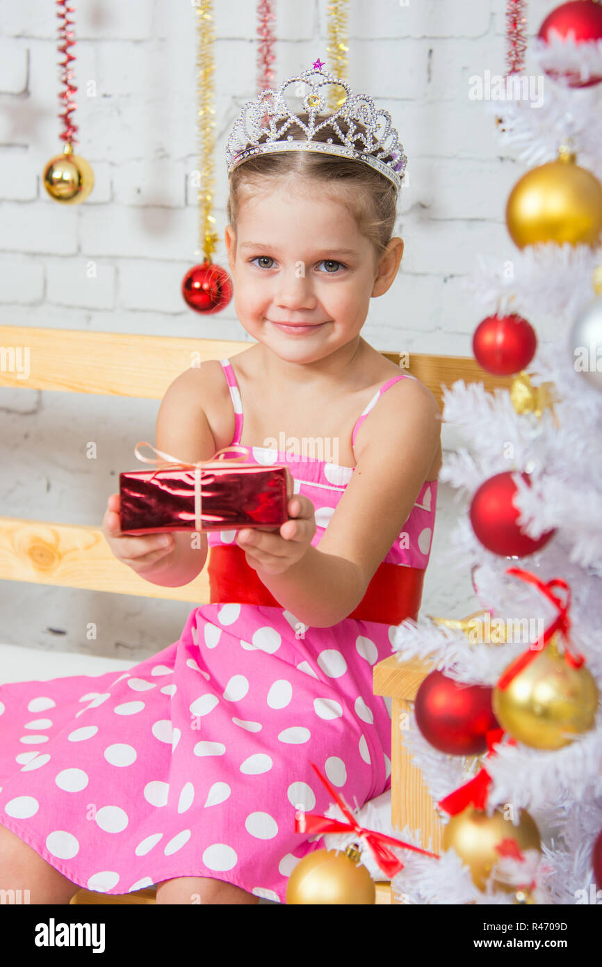 Vierjährige Mädchen erstreckt sich nach vorn ein kleines Geschenk sitzen verschneite Weihnachtsbäume Stockfoto