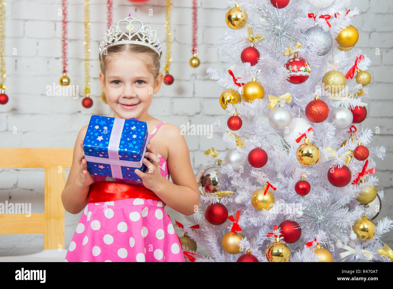 Glückliches kleines Mädchen hält ein Weihnachtsgeschenk und stehen in der Nähe von Weihnachtsbäumen Stockfoto