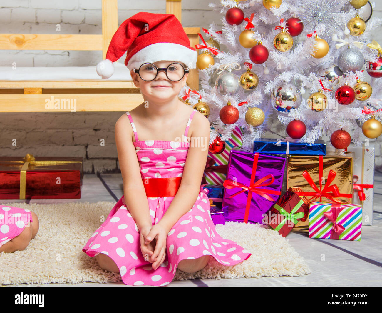 Mädchen, die in der Red Hat und die lustige Runde Gläser sitzt auf der Matte an der Weihnachtsbäume Stockfoto