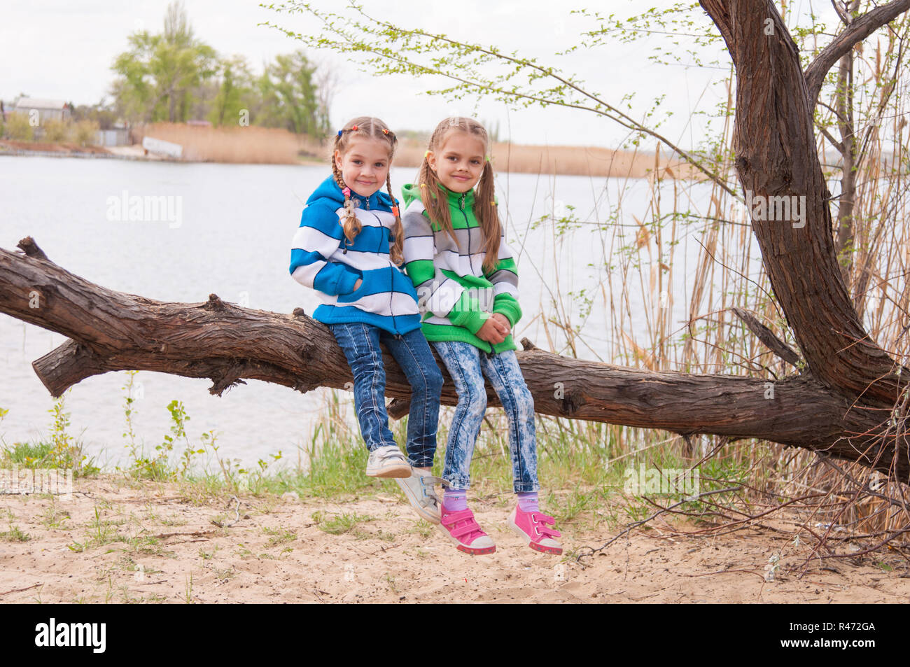 Zwei Mädchen sitzen auf einen umgestürzten Baum am Ufer Flusses Stockfoto