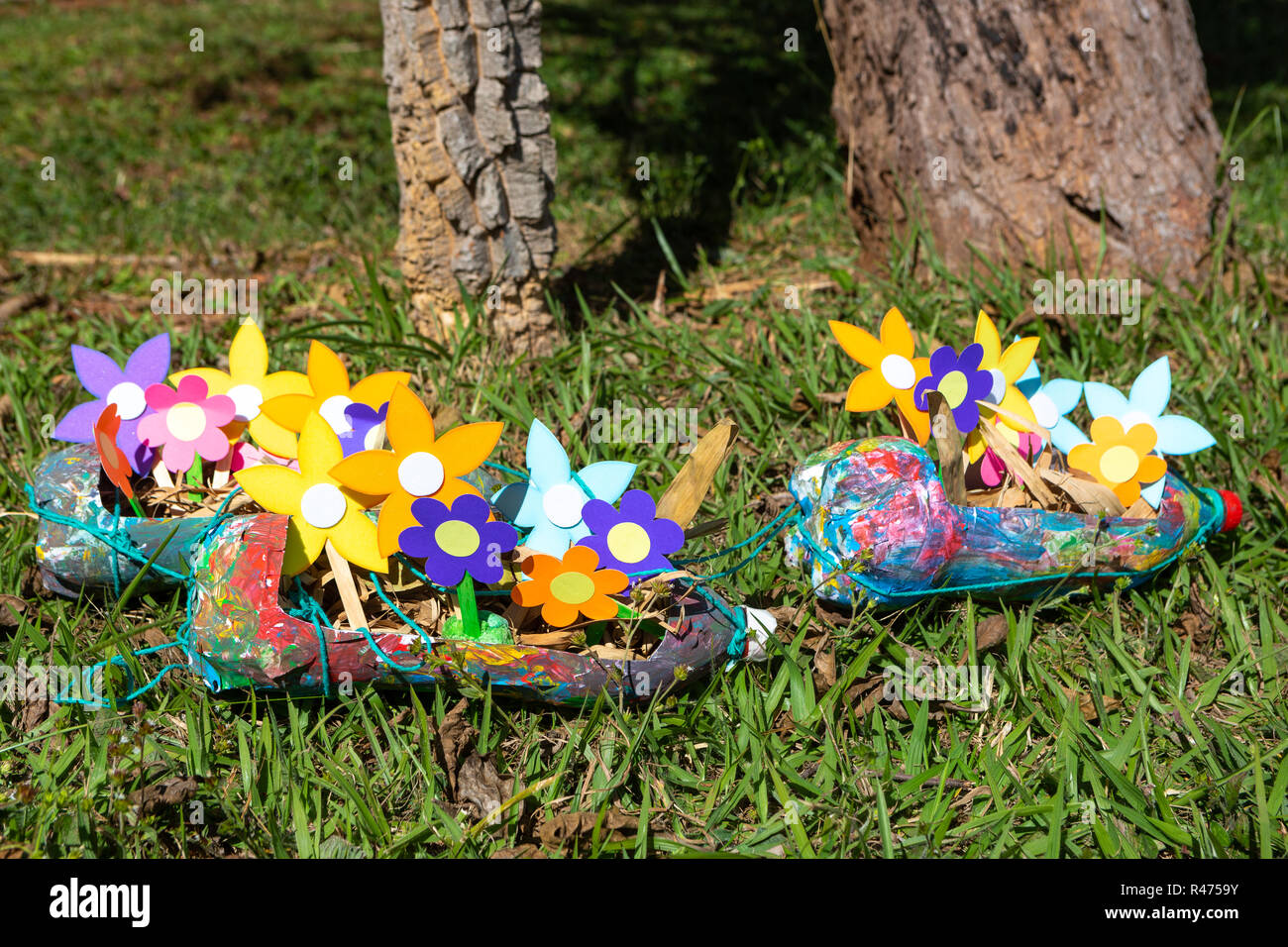 In der Nähe der bunten Papier Blumen im Pflanzer aus PET Flaschen in Gras garten. Stockfoto