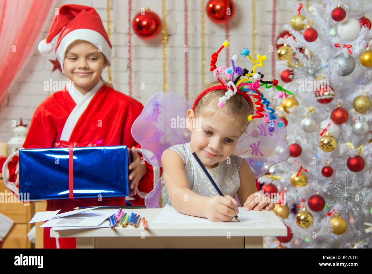 Mädchen sitzt an einem Tisch mit Feuerwerk auf dem Kopf, Santa Claus bereitet, sie zu überraschen Stockfoto