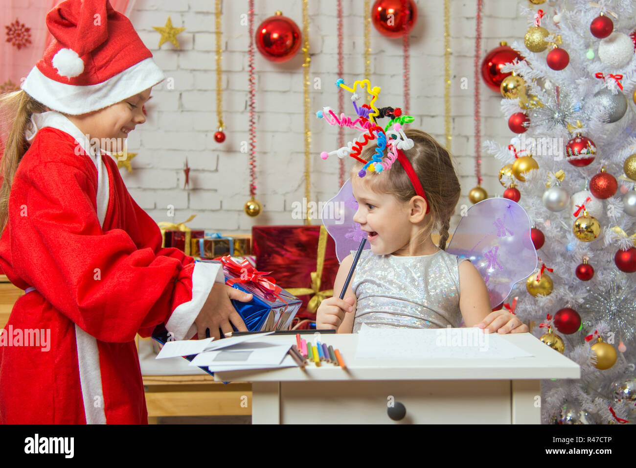 Mädchen sitzt an einem Tisch mit einem Feuerwerk auf dem Kopf, Weihnachtsmann gab ihr ein Geschenk Stockfoto