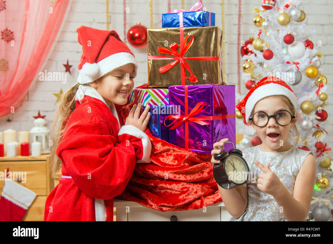 Mädchen mit Überraschung zeigt auf die Uhr in das neue Jahr, Santa Claus, lächelnd, glücklich Auspacken Geschenke Stockfoto
