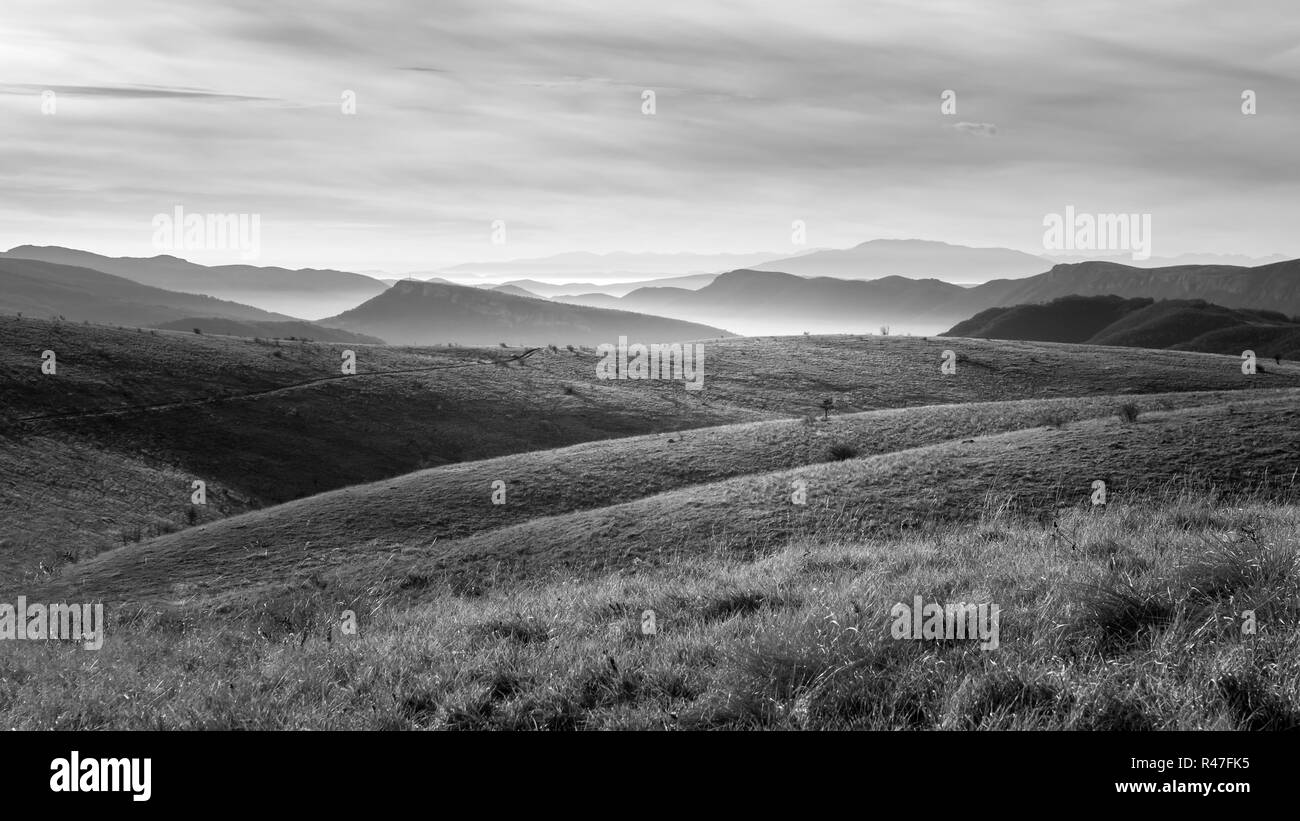 Beeindruckende Schwarz-Weiß-Ansicht von Formen der endlosen, weich, Misty Mountain Schichten, Vordergrund Gras und Dramatischer Himmel Stockfoto