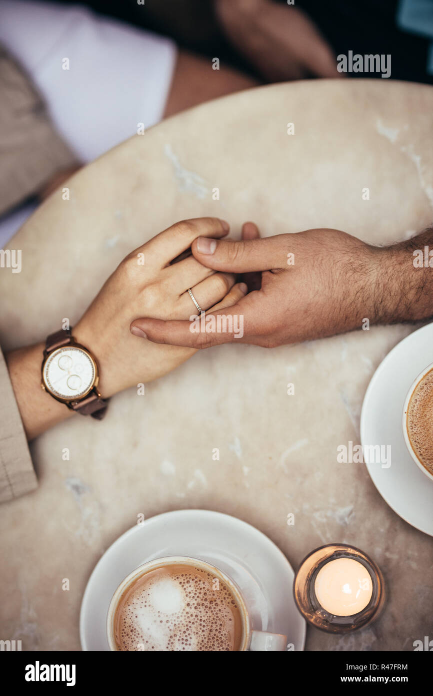 In der Nähe der Hände ein romantisches Paar gemeinsam an einem Tisch. Hände von ein paar jedes andere Holding mit Kaffee Tassen auf dem Tisch. Stockfoto