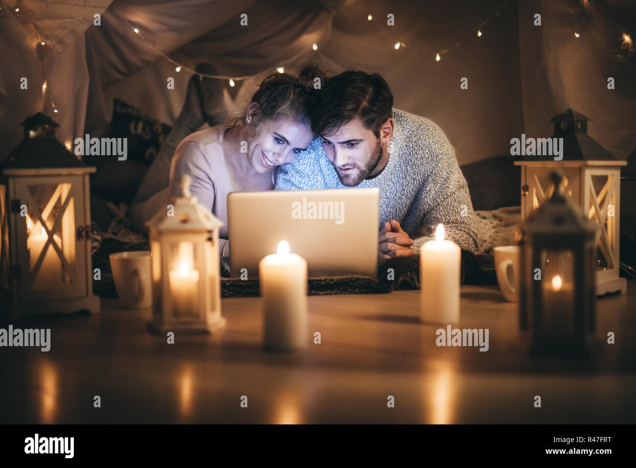 Mann und Frau auf dem Bett liegend einen Film auf Laptop in der Nacht in einem dekorierten Zimmer. Paar mit Laptop auf dem Bett in der Nacht mit Kerzen brennen Stockfoto