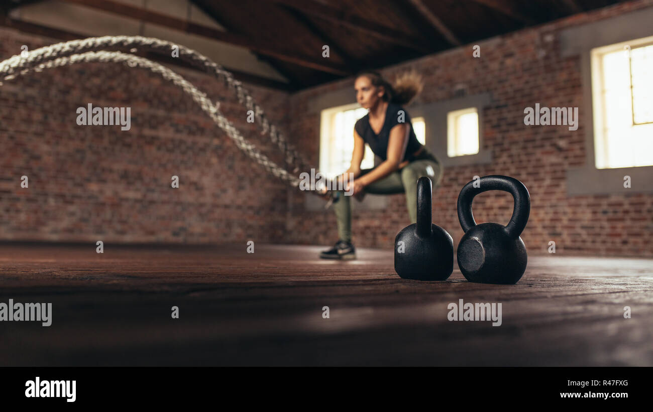 Wasserkocher Glocken auf dem Boden vor und Frau Trainieren mit Schlacht Seil. Weibliche trainieren Cross Training Gym. Stockfoto