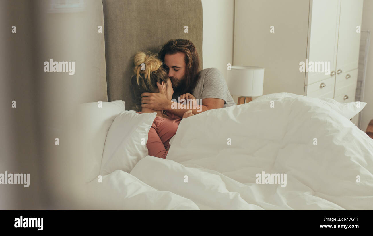 Mann und Frau liegend auf Bett zu Hause Zeit miteinander zu verbringen. Mann küsste seine Frau im Bett zu Hause liegen. Stockfoto
