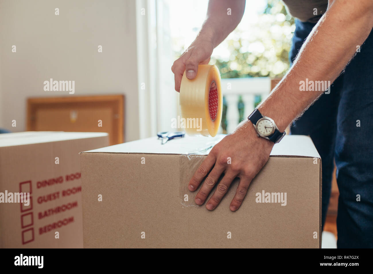 Der Mensch seine Hausrat in Umzugskartons und Abdichtung mit Klebeband. Stockfoto
